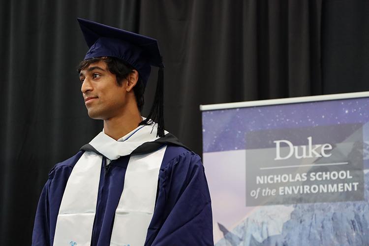 Rishab in academic regalia in front of Nicholas School banner