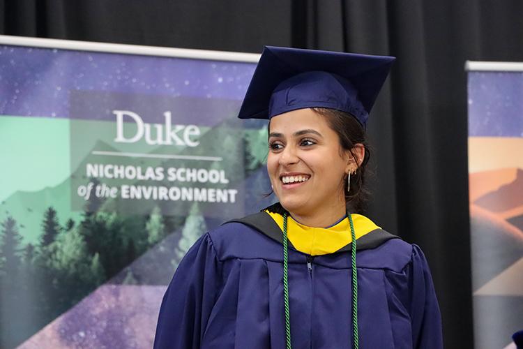 Anya on stage in academic regalia in front of Nicholas School banner