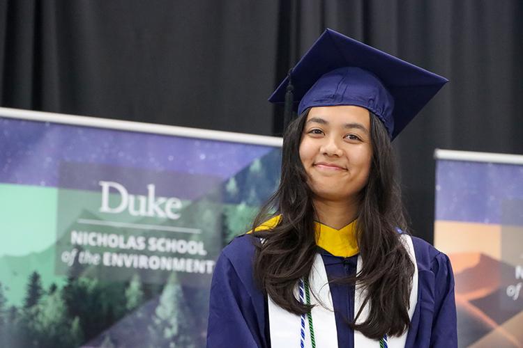 Emily in academic regalia in front of Nicholas School banner