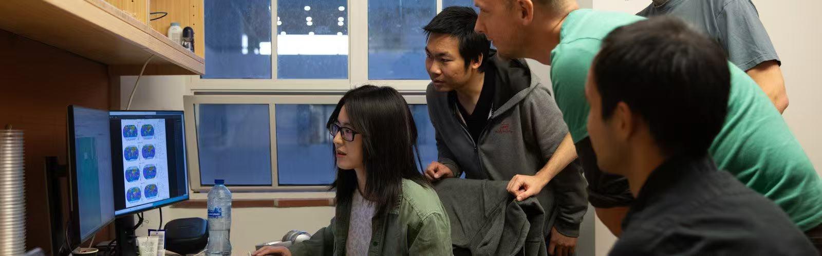 Liyin He sits at a computer surrounded by three individuals