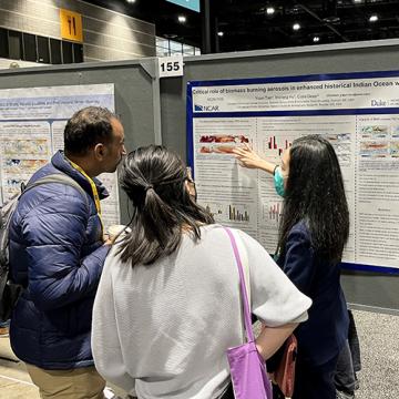 Yiqun presenting research poster to two people at AGU